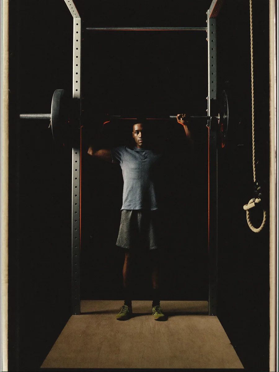 An athlete mid-set in a dark studio gym, dramatic side lighting with a subtle coral rim light, shot on 35mm, moody, cinematic, near-black background