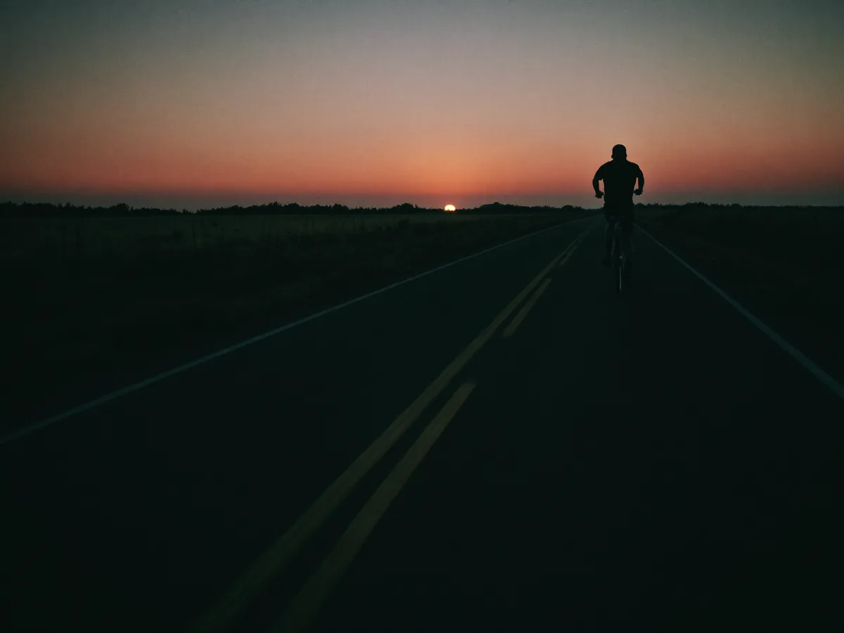 A lone runner at dawn on an empty road, cool dark tones with a coral sunrise accent, sense of motion, cinematic, minimal